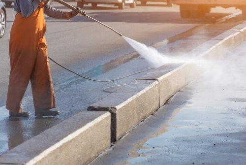 Worker cleaning driveway with gasoline high pressure washer splashing the dirt, asphalt road border. High pressure cleaning. Worker cleaning driveway with gasoline high pressure washer splashing the dirt, asphalt road border. High pressure cleaning