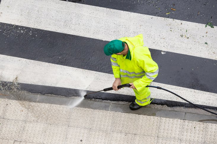 Worker cleaning a street sidewalk with high pressure water jet. Public maintenance